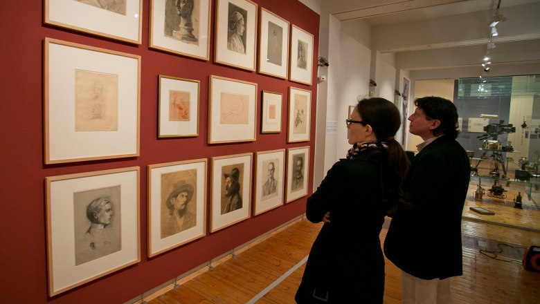 Egon Schiele Museum, © DanielHinterramskogler Two people look at drawings on a red wall in a museum.