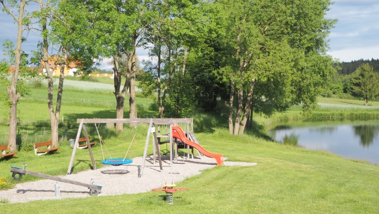 Playground, © MG Sallingberg Playground with swing, slide and seesaw next to a pond in a green landscape.