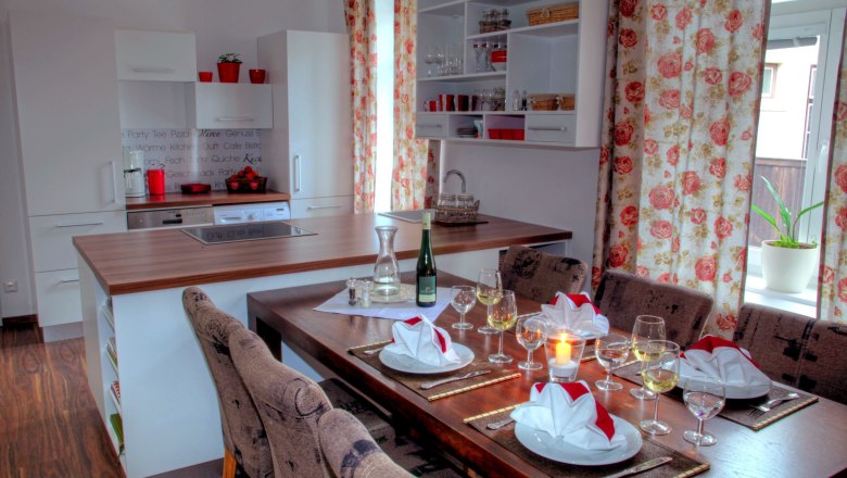 Kitchen in loft 1, © Carlos de Mello Modern kitchen with dining table, set with glasses and napkins, floral pattern curtains.