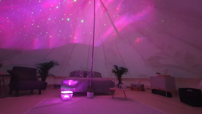 Glamping - Wilderness Center Nasswald, © Jonathan Clark Interior view of a glamping tent with pink lighting and cozy furnishings.