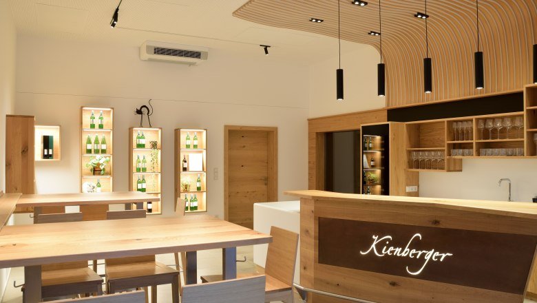 Tasting room, © Sophie Kienberger Modern tasting room with wooden furniture and illuminated shelves with bottles.