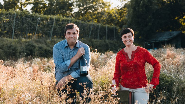 hofmann-2022, © David Schreiber Two people in a vineyard, one holding a wine bottle, the other a wine glass.