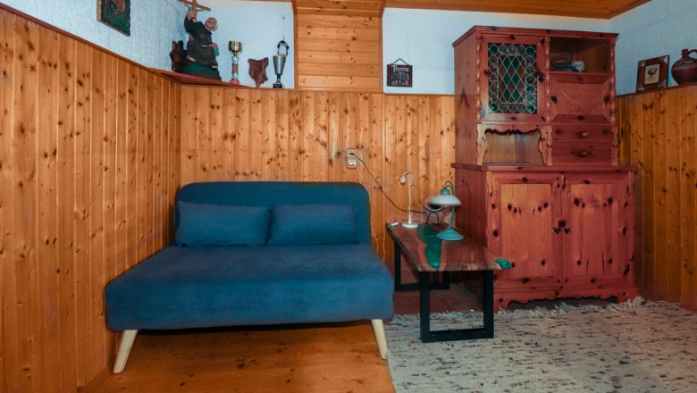 Extra bed in the parlor, © Novasol / Fam. Schachner Cozy room with wooden walls, a blue sofa, a wooden table and a rustic wardrobe.