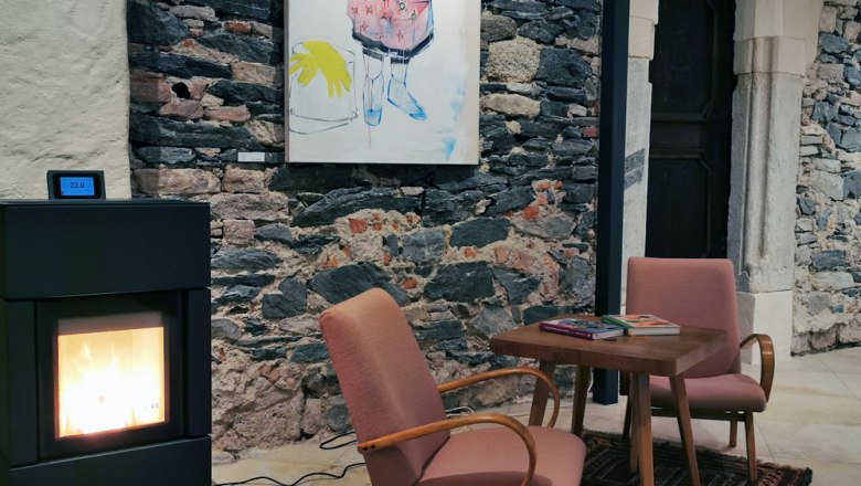 Salon-77 Agapitus Room, © Marlene Bergkirchner Cozy room with fireplace, two armchairs, table and artwork on a stone wall.