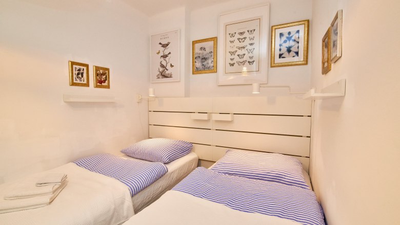 Top 3 - Bedroom, © VP FeWo OG Two single beds with blue striped bed linen in a bright bedroom with decorative pictures on the wall.
