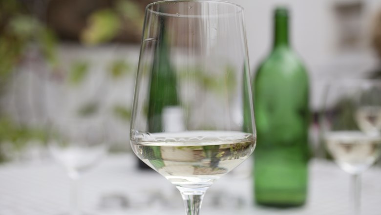 Wine glass, © Weinviertel Tourismus / Christine Wurnig A wine glass with white wine in the foreground, blurred green wine bottle in the background.