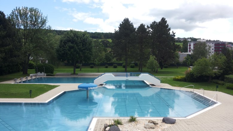 Basin, © Dagmar Ackerl An empty outdoor pool with several pools, surrounded by trees and lawns, under a cloudy sky.