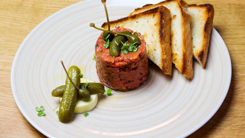Beef tartar-arranged, © Weingut Nigl Beef tartare with capers, gherkins and toast on a plate.