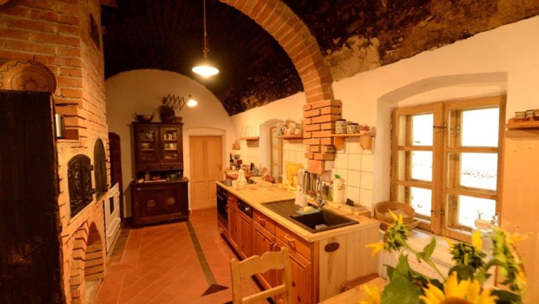 Kitchen - Mariahaus, © Martina Heilingsetzer Rustic kitchen with brick arch, wooden furniture and sunflowers on the table.