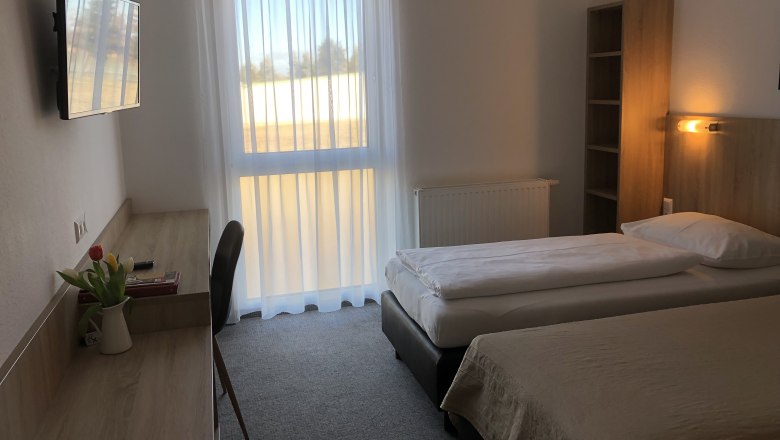 Amber Motel, © Bernstein Motel A simply furnished motel room with two single beds, a desk, a TV and a window with curtains.