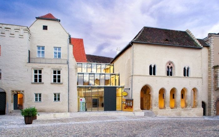 Gozzoburg, © Birgit Lechner Historic building with a modern glass intermediate structure, cobblestones in the foreground.