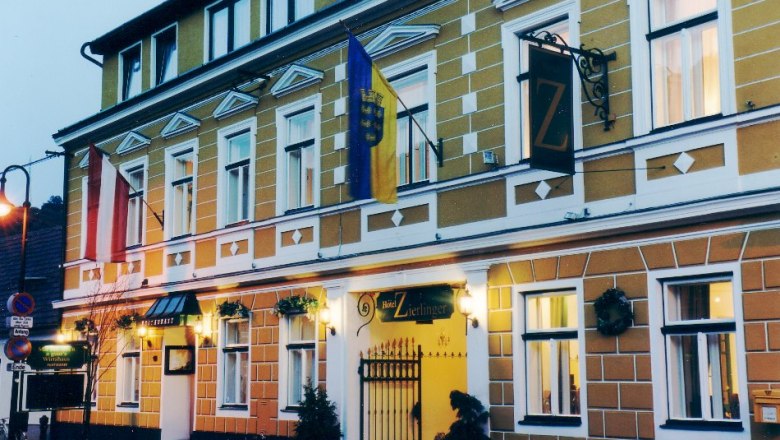 Hotel picture, © Eigenes Foto Exterior view of the Hotel Zierlinger with yellow façade and flags.