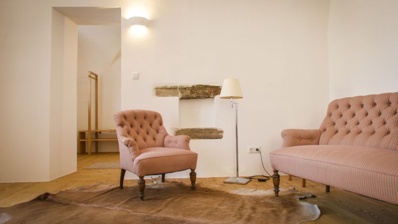 Oberstockstall Estate, © Robert Herbst A cozy living room with an armchair, a sofa, a floor lamp and a carpet on a wooden floor.