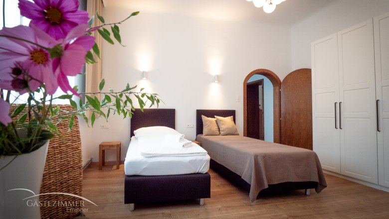 Double room, © Doris Eminger A cozy twin room with flowers in the foreground, two beds, a wardrobe and a lamp on the ceiling.