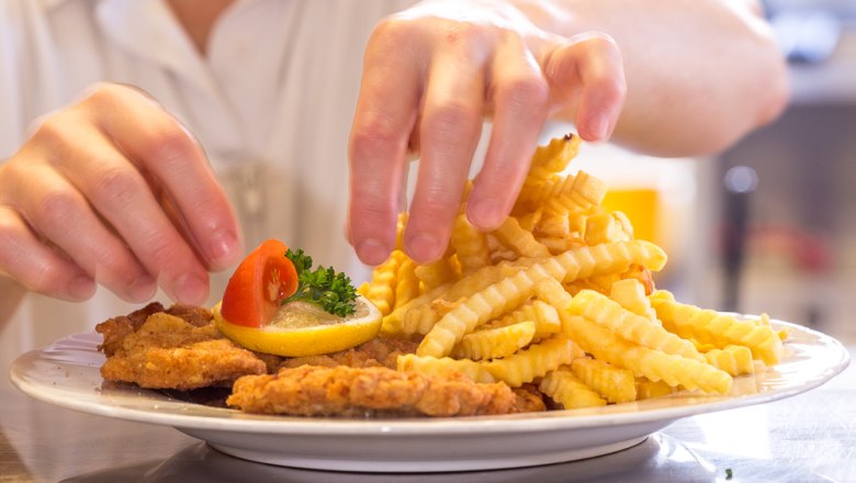 Wiener schnitzel with fries, © Foto Weidinger A plate with Wiener Schnitzel, French fries, lemon and tomato is served by one person.