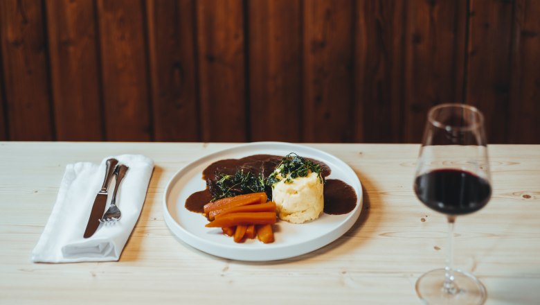 Braised beef cheeks, truffled mashed potatoes, glazed carrots, © Niederösterreich Werbung/David Schreiber Elegant dish with meat, vegetables and red wine on a wooden table.