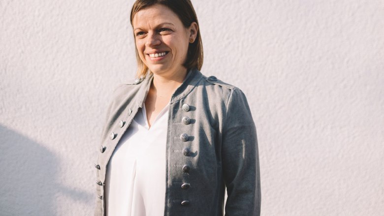 In service: Sandra Buchinger-Löfler, © Niederösterreich Werbung/Mara Hohla Woman in a gray jacket in front of a white wall.