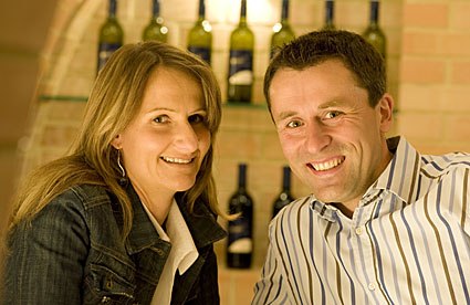 Winegrower couple, © Mold A smiling couple in a wine cellar with bottles of wine in the background.