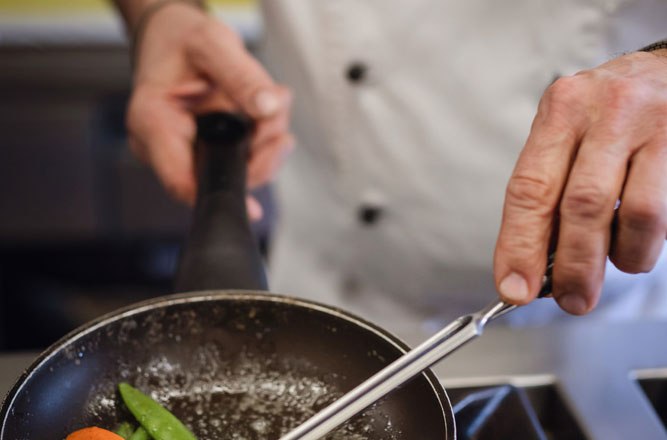 Award-winning cuisine on the Moststraße, © Niederösterreich Werbung/Daniela Führer A cook in a white uniform fries vegetables in a pan on a gas stove.
