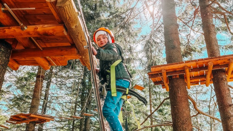 Hirschenkogel forest ropes course Semmering, © Semmering-Hirschenkogel A child wearing a helmet and safety equipment climbs between trees in a forest ropes course.