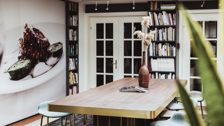 Living a culture of enjoyment, © Niederösterreich Werbung/David Schreiber Modern room with large table, bookshelves and mural.