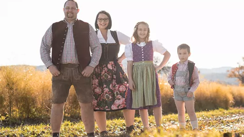 Vitamin Hedgehog's, © Vitamin Igels A family with two children dressed in traditional costume is standing on a path in front of a field.