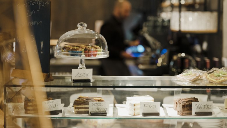 Cakes from our own patisserie, © Niederösterreich Werbung/Michael Reidinger Confectionery with cakes and muffins in a glass display case, offer board in the background.