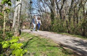 3 footbridges, Kleine Au, Fischamend, © Donau Niederösterreich, Neubauer A couple walks along a path in a wooded park.