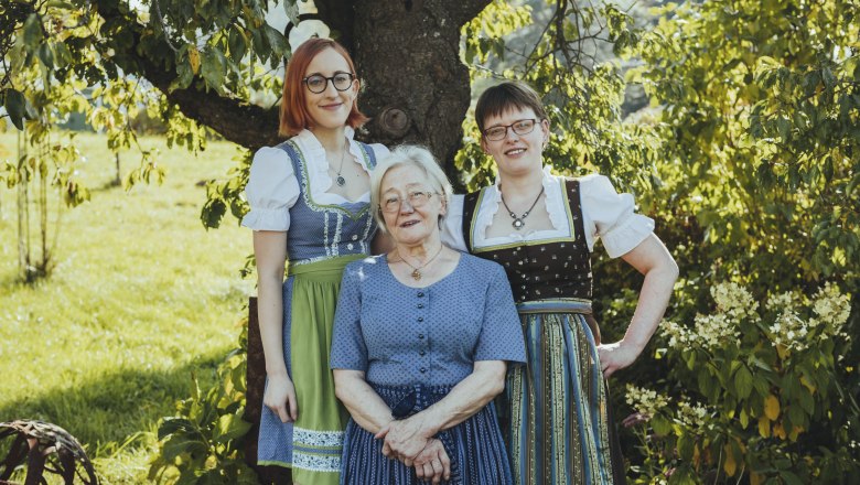Intergenerational women's power, © Niederösterreich Werbung/David Schreiber Three women in traditional costume stand smiling under a tree outside.