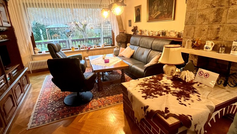 Heidi's Place living room, © Wiener Alpen Cozy living room with leather sofa, armchair, wooden table and fireplace. Large window front with view to the outside. Rustic furnishings with carpet.