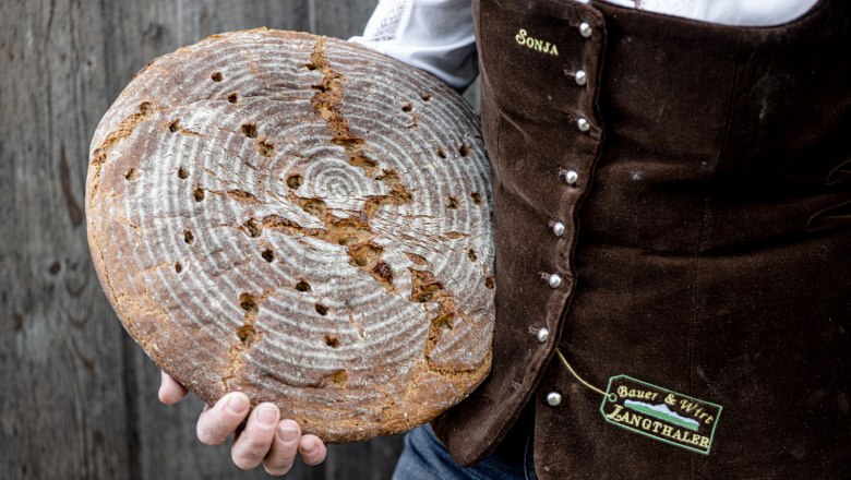 Fresh home-baked bread, © Martina Siebenhandl Person holds round, home-baked bread in front of a rustic background.