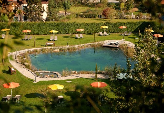 Organic swimming pond, © Residenz Wachau A natural swimming pond with sun loungers and colorful parasols on a green meadow.