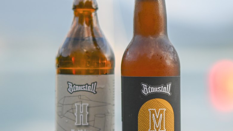 brewery-beer-mondsee, © Hofbrauerei Braustall_Georg Schwameis Two beer bottles from Braustall on a wooden table in front of a blurred background.