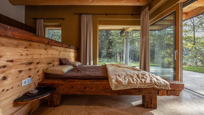 Vacation home by the lake, © Niederösterreich Werbung / Maximilian Pawlikowsky Rustic bedroom with wooden bed and large windows with a view of nature.