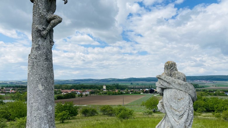 Calvary vineyard, © Weinstraße Weinviertel Two stone sculptures on a hill with a view of a rural landscape and a village in the background.