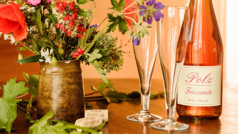 Winery Polz, © Rita Newman A bottle of Polz Frizzante with two glasses and a bouquet of flowers on a table.