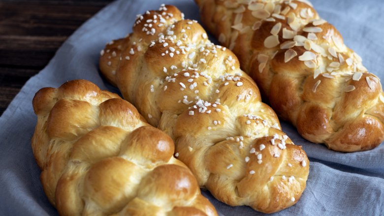 Briochstrizel, © Fam. Luckerbauer Three braided brioche striezel on a blue cloth, one sprinkled with almonds, one with sugar crystals.