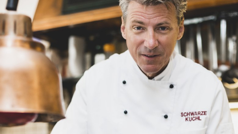 Landlord Andreas Macher, © Niederösterreich Werbung/David Schreiber Cook in white uniform in a kitchen with copper lamp.