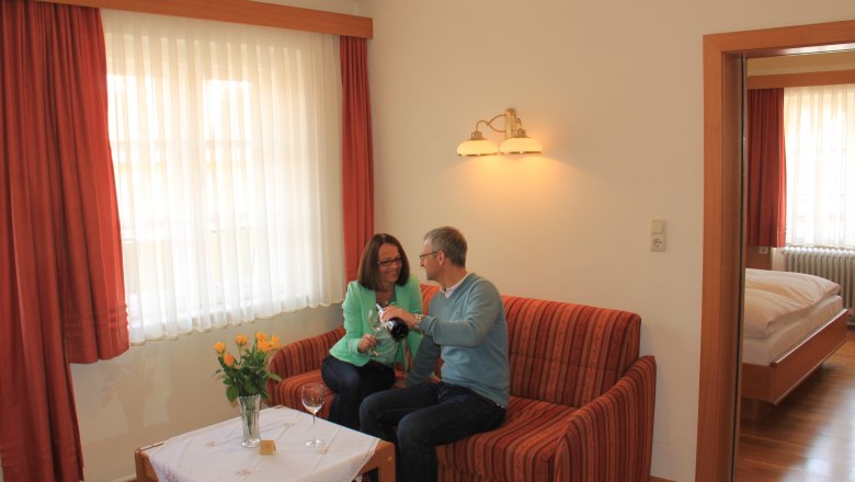 Apartment, © Schendl A couple sits on a sofa in a cozy apartment and pours wine.