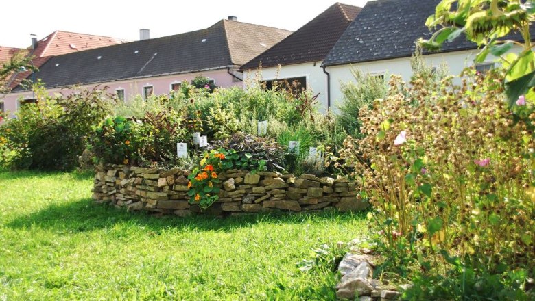 herb_bed_2_small__herb_village_merkenbrechts, © Kräuterdorf Merkenbrechts Herb bed with stone wall in a garden in front of houses.