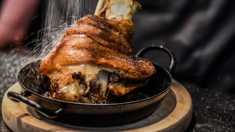 Hofbräu at the Steinertor, © Extra Krems Crispy pork knuckle in a pan on a wooden board, sprinkled with salt.