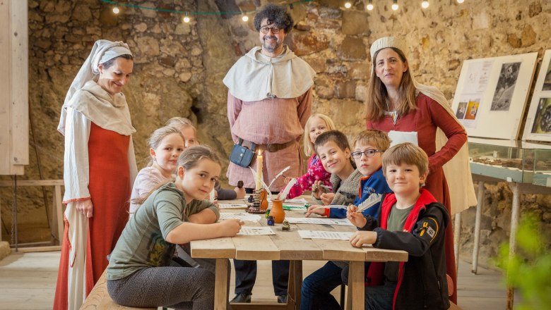 Children's program, © Manfred Kubanik Children and adults in medieval dress at a table in a ruined castle.