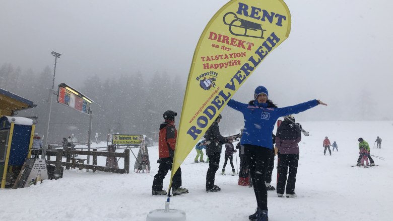 Dagmar Beachflag tobogganing, © Happylift Semmering Person in the snow next to a yellow beach flag with the inscription 'Toboggan rental'.