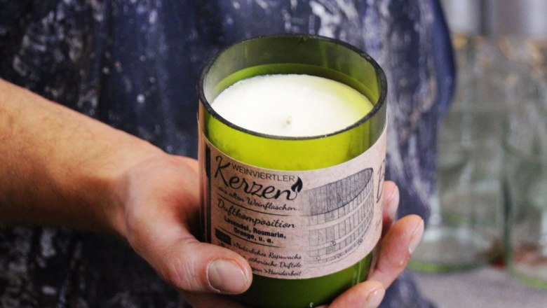Candle manufactory, © Glaser Kerzen One hand holds a green scented candle with the label 'Weinviertler Kerzen'.
