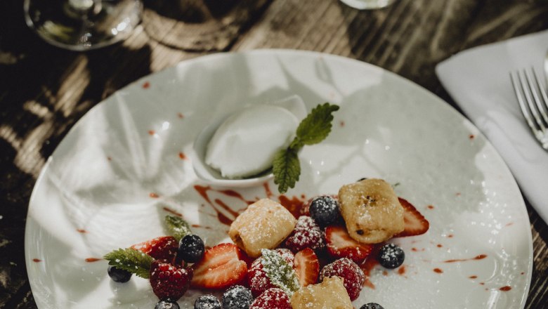 Baked curd cheese with marinated berries & yoghurt ice cream, © Niederösterreich Werbung/Sophie Menegaldo A dessert plate with baked curd cheese, marinated berries and yoghurt ice cream, decorated with mint leaves, on a wooden table.