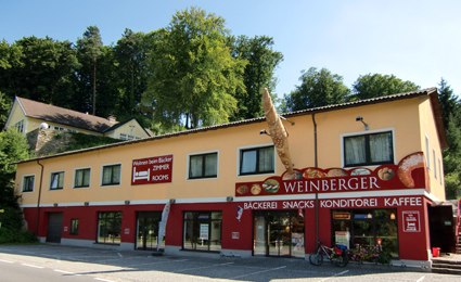 Exterior view, © Weinberger Exterior view of a bakery with yellow facade and red sign.