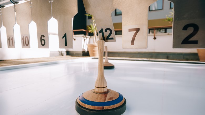 Curling, © Sporthotel Semmering Curling on a smooth surface in front of numbered targets.