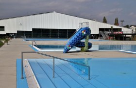 Florian Berndl Bathroom, © Marktgemeinde Bisamberg An empty outdoor pool with a colorful slide and a large building in the background.