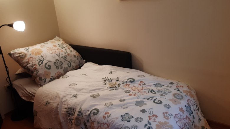 Room with an extra bed, © Kainz-Waldinger A small room with a single bed covered with a flowered bedspread. A floor lamp stands next to it and a colorful picture hangs on the wall.