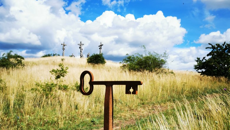 Perfect photo spot on the Calvary, © Weinstraße Weinviertel A photo point sign in front of a meadow with three crosses in the background under a blue sky with clouds.